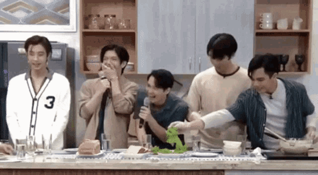 a group of young men are standing in a kitchen with a microphone .