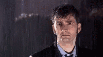 a man in a suit and tie is standing in the rain with a sad look on his face .