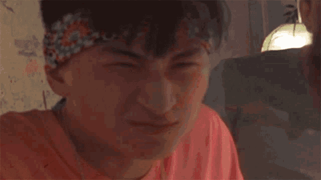 a man with a bandana on his head is covering his mouth with his hand