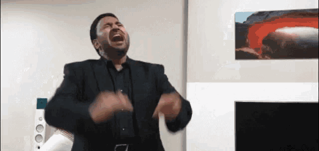 a man in a suit is screaming in a living room with a picture of a volcano on the wall behind him .