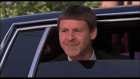 a man with a very short haircut is smiling while sitting in a car
