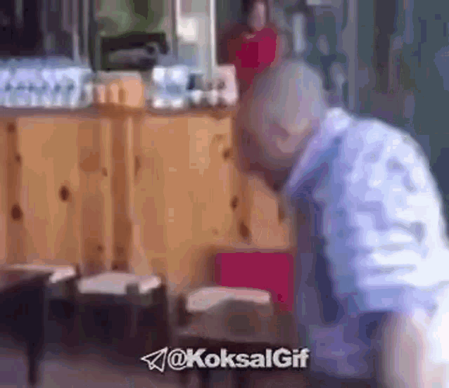 a man in a blue shirt is standing in front of a wooden counter and chairs .