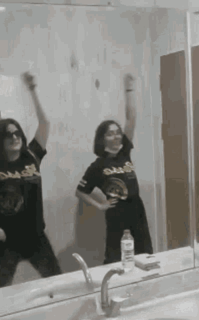 two women are dancing in front of a mirror with one wearing a shirt that says oasis