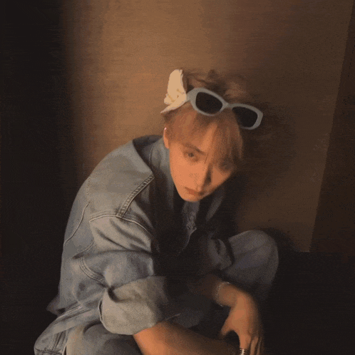 a young man wearing a denim jacket and sunglasses looks at the camera