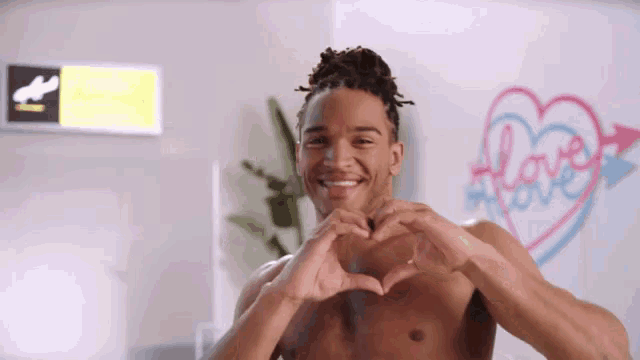 a shirtless man making a heart with his hands in front of a sign that says love
