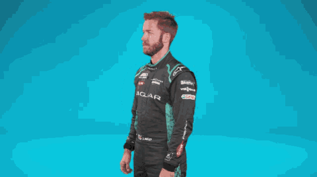 a man in a jaguar racing suit is standing with his arms crossed