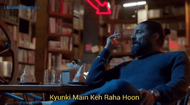 a man sitting at a table with the words kyunki main keh raha hoon written on the bottom