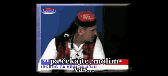 a man in a black hat is talking on a television screen with the words " vipa cekajte molim vas "