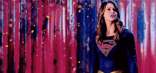 a woman in a supergirl costume is standing in front of a pink wall .