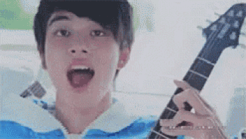 a young man is holding a guitar with his mouth open and making a funny face .
