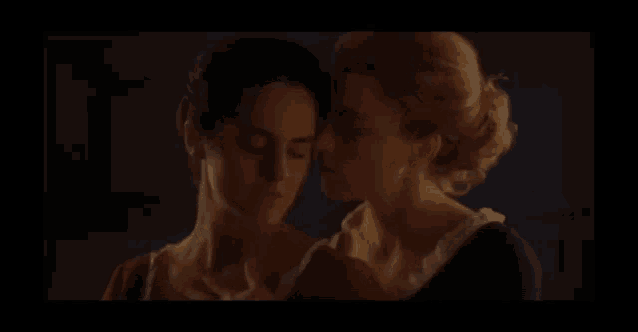 two women are standing next to each other in a dark room and kissing .