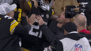 a man wearing a nfl jacket holds a football player 's chest
