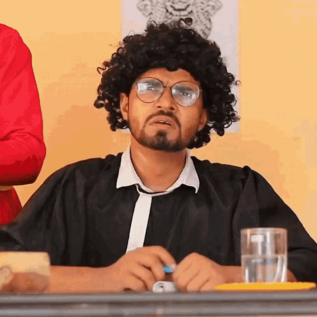 a man wearing glasses and a wig is sitting at a table