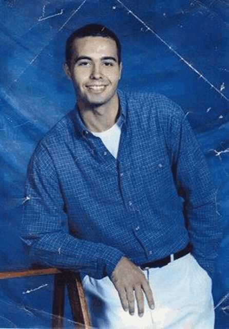 a man in a blue shirt and white pants is leaning on a stool .