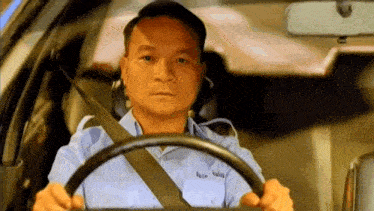 a man in a blue shirt is driving a car with a seat belt on