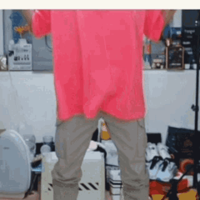 a man in a pink shirt and khaki pants is standing in a room with a lot of shoes on the floor .