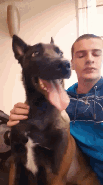 a man in a blue sweatshirt is holding a dog with its tongue hanging out