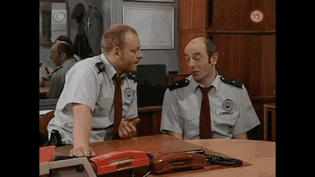 two men in uniform are sitting at a table talking to each other .