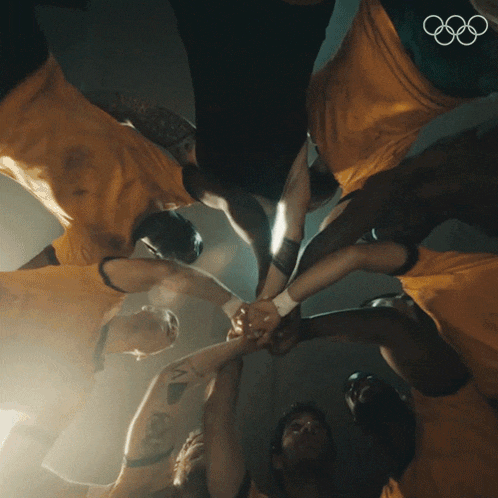 a group of people are putting their hands together in a circle with the olympic rings in the background