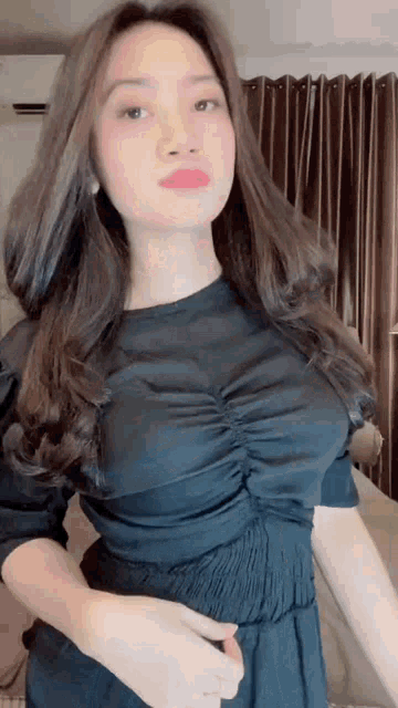 a woman in a black dress is standing in front of a brown curtain .