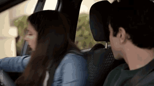 a man and a woman are sitting in the back seat of a car talking to each other .