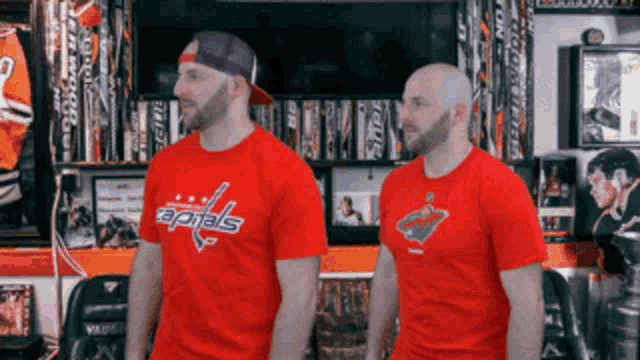 two men standing next to each other wearing red capitals t-shirts