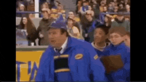a man in a blue jacket and hat is standing in front of a crowd of people at a hockey game .