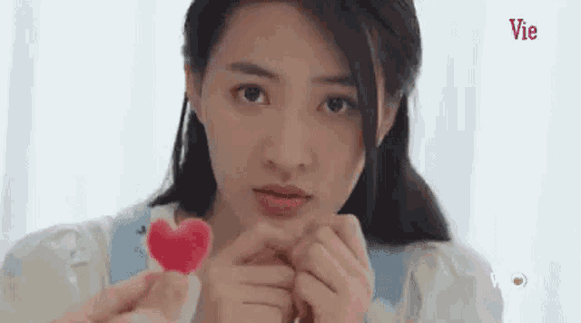 a woman is holding a red heart in her hands and looking at the camera .