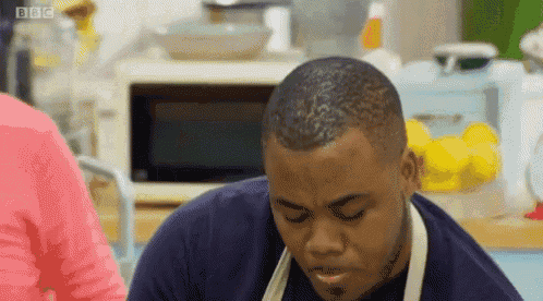 a man wearing an apron is sitting at a table with his eyes closed and his mouth open .