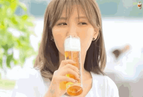 a young woman is drinking a glass of beer from a tall glass .