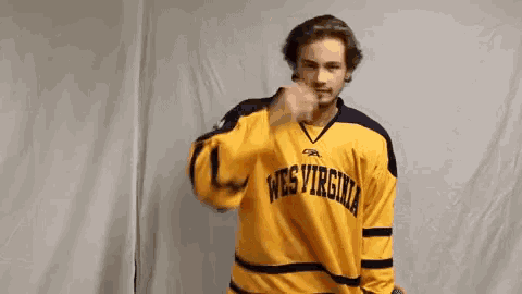a man wearing a yellow west virginia hockey jersey is holding his head .