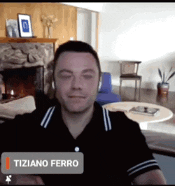 a man sitting in front of a fireplace with the name tiziano ferro on the bottom right