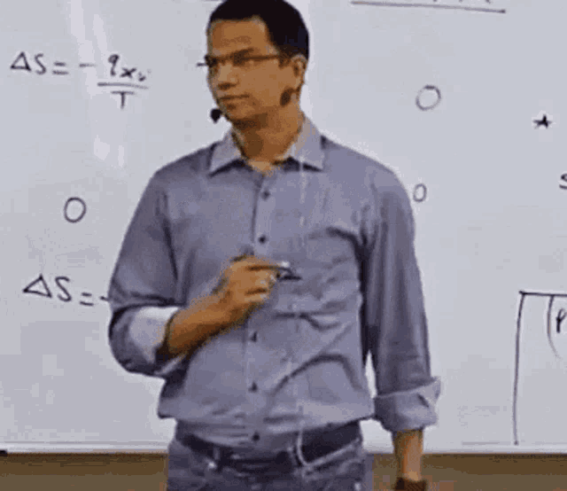 a man in a blue shirt is standing in front of a whiteboard with a microphone .
