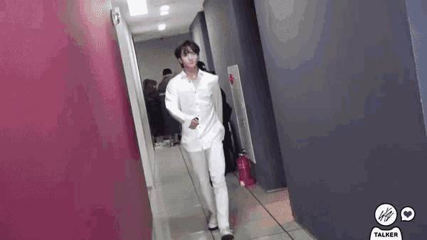 a man in a white shirt and white pants is standing in a hallway .