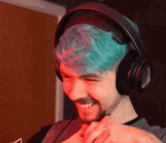 a man with blue hair and headphones is smiling and looking at his phone .