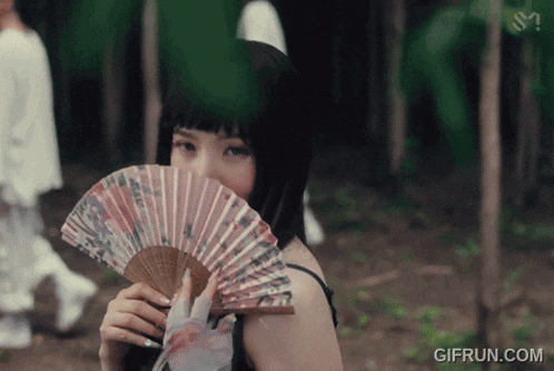 a woman holding a fan in front of her face with a gifrun.com watermark