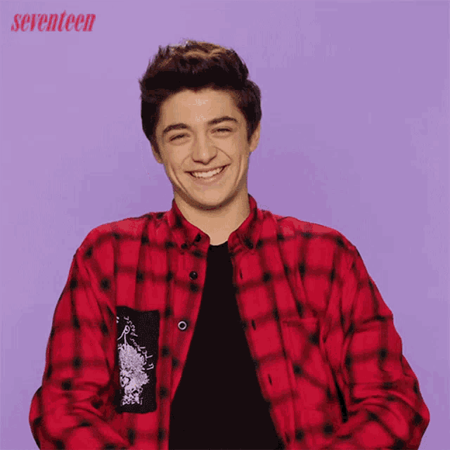a young man wearing a red plaid shirt is smiling in front of a seventeen logo