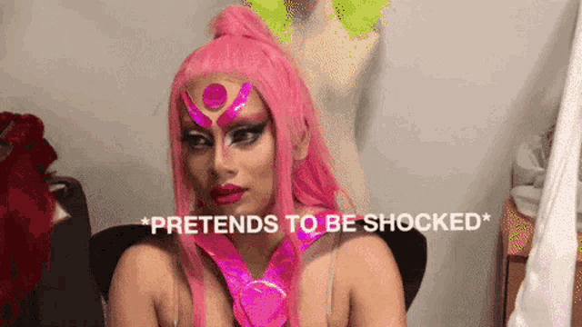 a woman in a pink wig is sitting in a chair with the words pretends to be shocked above her .