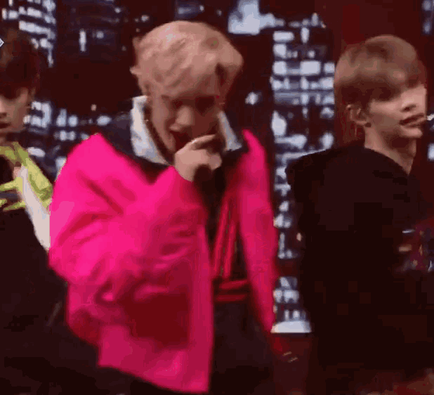 a man in a pink jacket is singing into a microphone while two other men look on .