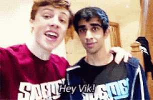 two young men are posing for a picture together and one of them is wearing a shirt that says `` hey vik '' .