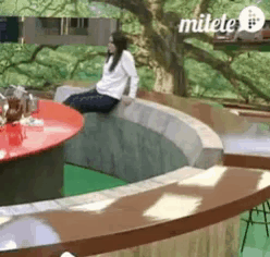 a woman is sitting on a ledge in front of a tree and the word milele is on the bottom right