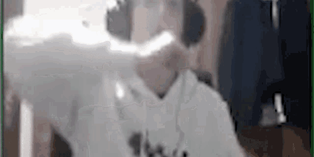 a man wearing headphones and a white hoodie is sitting in front of a green screen .