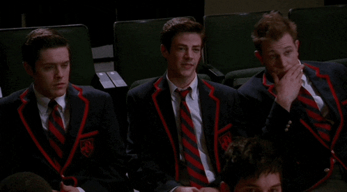 three men in suits and ties are sitting in a auditorium