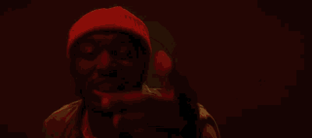 a man wearing a red beanie looks at the camera in a dark room