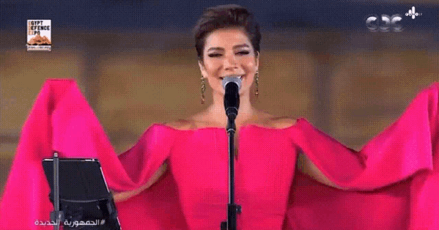 a woman in a red dress is singing into a microphone in front of an orchestra with a sign that says happy bitches cup