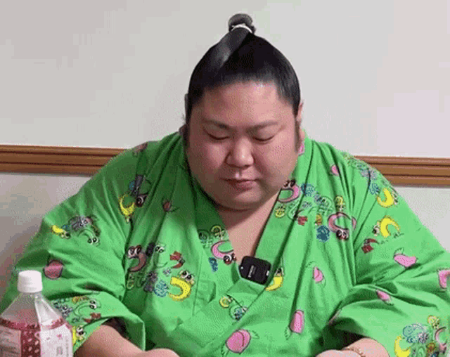 a man wearing a green kimono with a banana on it is sitting next to a bottle of water .