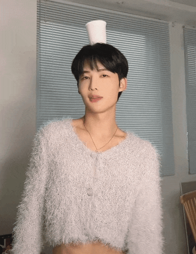 a young man wearing a white sweater with a cup on his head