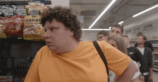 a man in an orange shirt is standing in front of a shelf with haribo candy on it