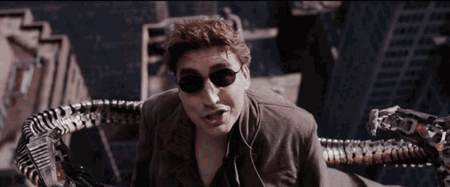 a man wearing sunglasses and a suit has a robotic arm coming out of his chest