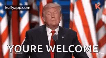 donald trump is giving a speech in front of american flags and says `` youre welcome '' .